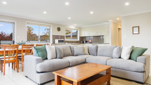 A modern living room with a grey sectional sofa, wooden coffee table, and a dining area with wooden chairs and a table.