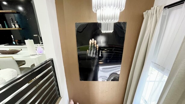 Un escalier moderne avec des finitions en bois, un miroir à cadre noir, un lustre et une vue sur une voiture à travers une fenêtre.