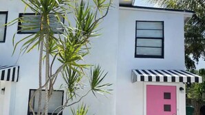 Un bâtiment moderne à deux étages, avec une façade blanche, des encadrements de fenêtres noirs et une porte rose.