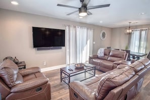 Ein Wohnzimmer mit Ledersofas, einem Flachbildfernseher, einem Deckenventilator und einem Essbereich mit Tisch und Stühlen.