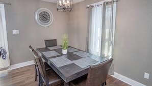 Comedor con una mesa rectangular, cuatro sillas, una planta en maceta, un reloj de pared y una lámpara de araña.