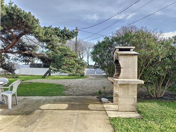 A patio area with a concrete bench, a stone structure, and a grassy lawn. - VILLA SOLEIL (La Brée-les-Bains)
