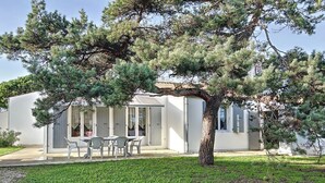 A modern house with a covered patio, a dining area, and a large tree in the foreground. - VILLA SOLEIL (La Brée-les-Bains)