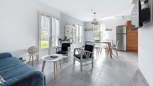 A modern living room with a blue sofa, a dining area with chairs and a table, and a kitchen with a refrigerator and cabinets. - VILLA SOLEIL (La Brée-les-Bains)