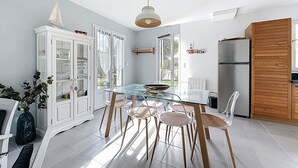 A modern kitchen with a glass dining table, wooden chairs, a white cabinet, and a wooden cabinet with a ship decoration. - VILLA SOLEIL (La Brée-les-Bains)