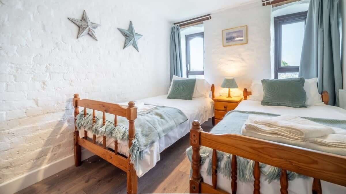 Una habitación con dos camas de madera, una pared de ladrillo blanco y dos ventanas con cortinas.