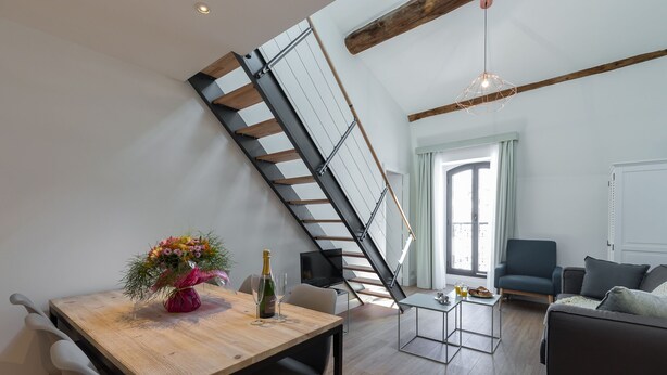 Un espace de vie moderne comprenant une table à manger en bois, un canapé, un téléviseur et un escalier doté d’une rampe en métal.