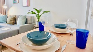 Een eetgedeelte met een houten tafel voor twee personen, met blauwe kommen, witte borden en glazen wijnglazen.