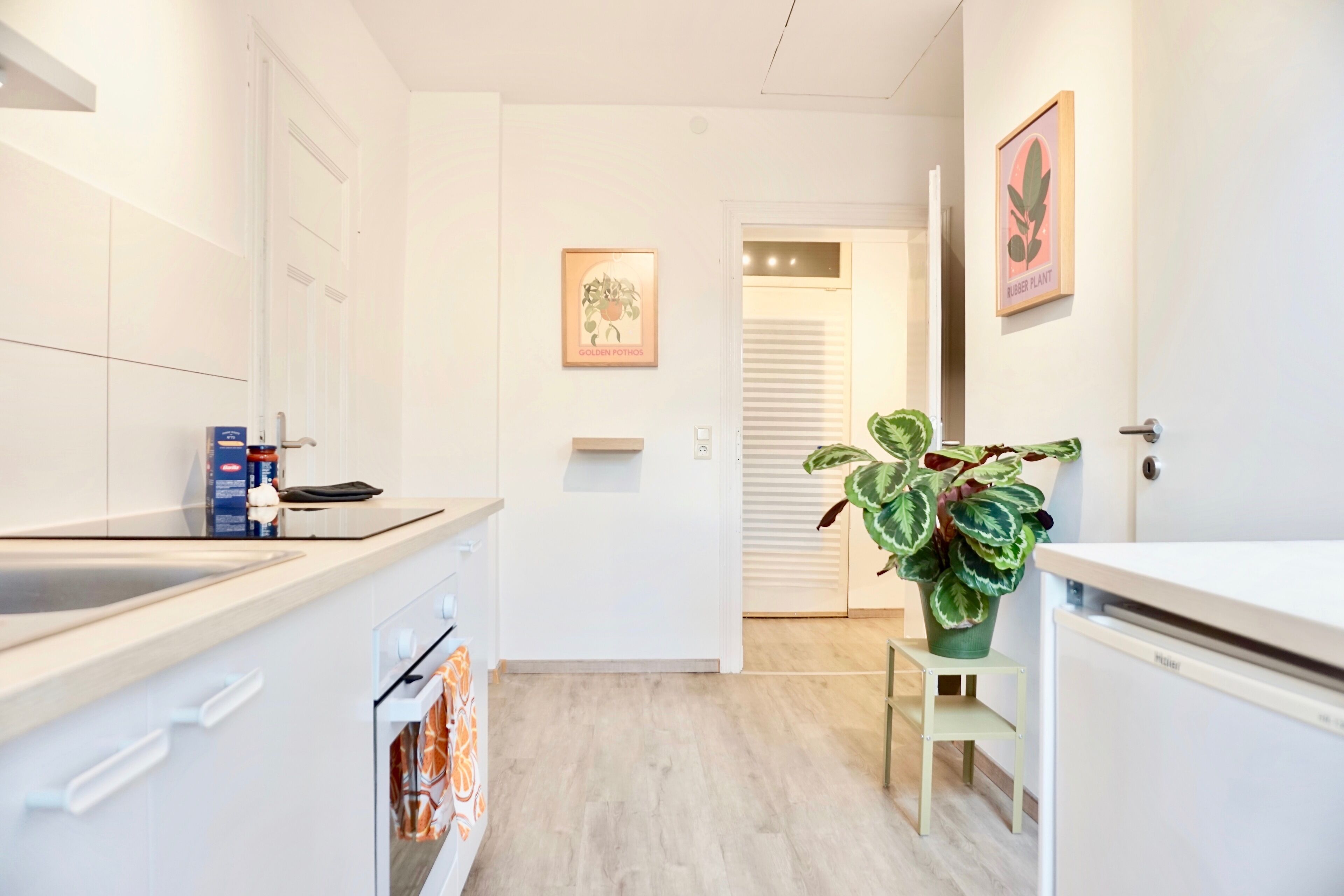Eine moderne Küche mit weißen Schränken, einem eingebauten Ofen und einer Arbeitsplatte mit Spüle. Neben der Spüle steht ein kleiner Tisch mit einem Blumentopf.