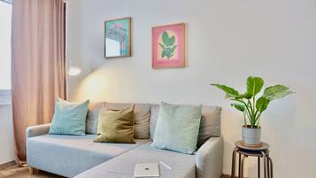 Una sala de estar moderna con un sofá gris, una mesita con una computadora portátil y una planta en maceta.