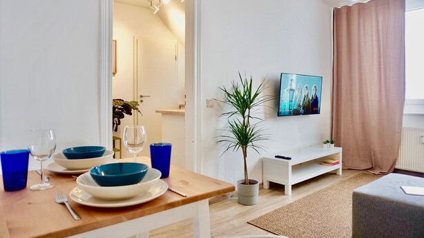 Een moderne woonkamer met een eethoek, een potplant, een flatscreen televisie en een witte televisiemeubel.