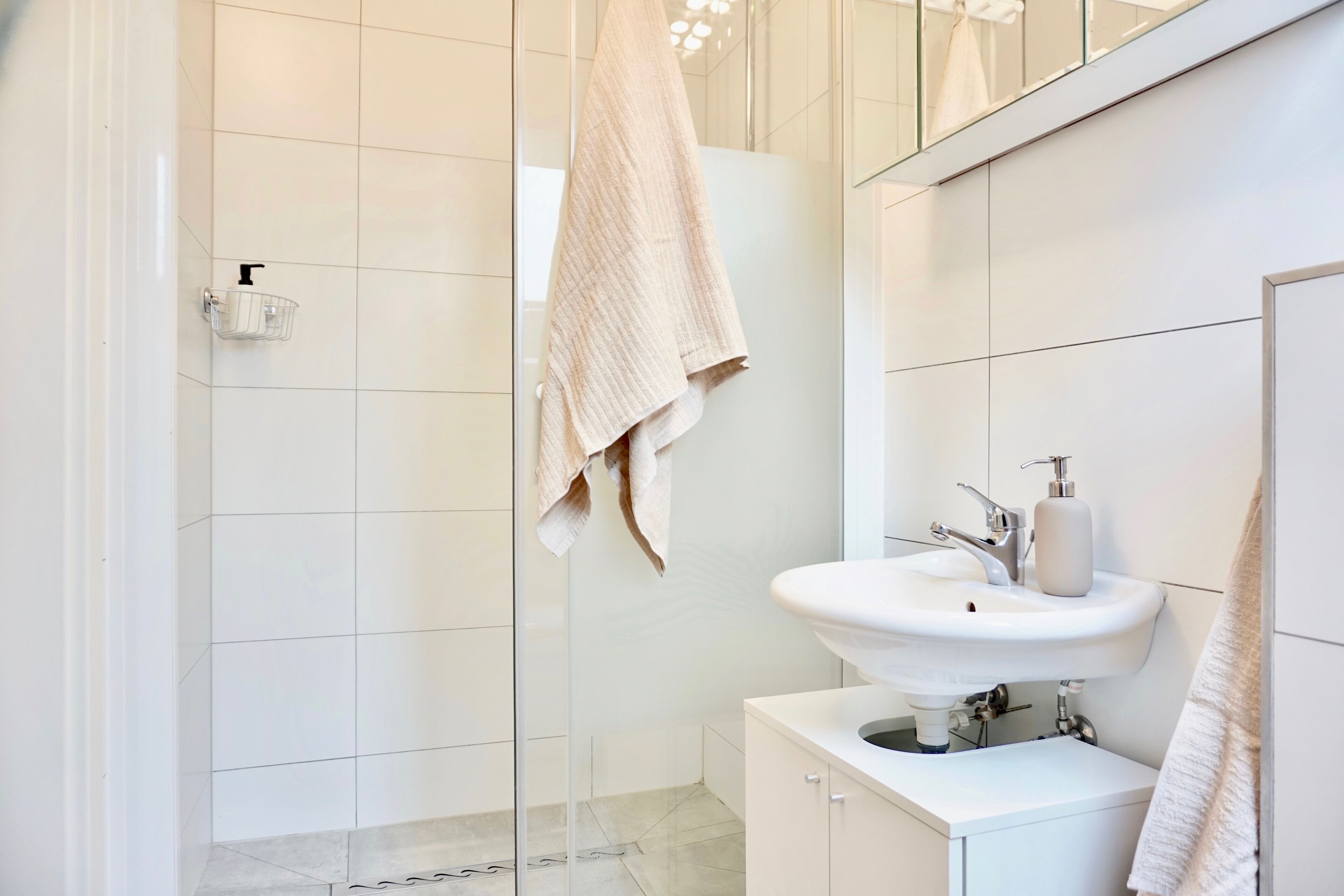 Ein modernes Badezimmer mit einem weißen Waschbecken, einer Duschkabine aus Glas und einem Handtuch an einem Wäscheständer.