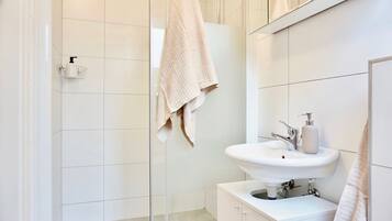 Ein modernes Badezimmer mit einem weißen Waschbecken, einer Duschkabine aus Glas und einem Handtuch an einem Wäscheständer.