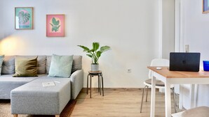 Ein modernes Wohnzimmer mit einem grauen Sofa, einem kleinen Holztisch mit einem Laptop, einer Topfpflanze und zwei gerahmten Bildern an der Wand.