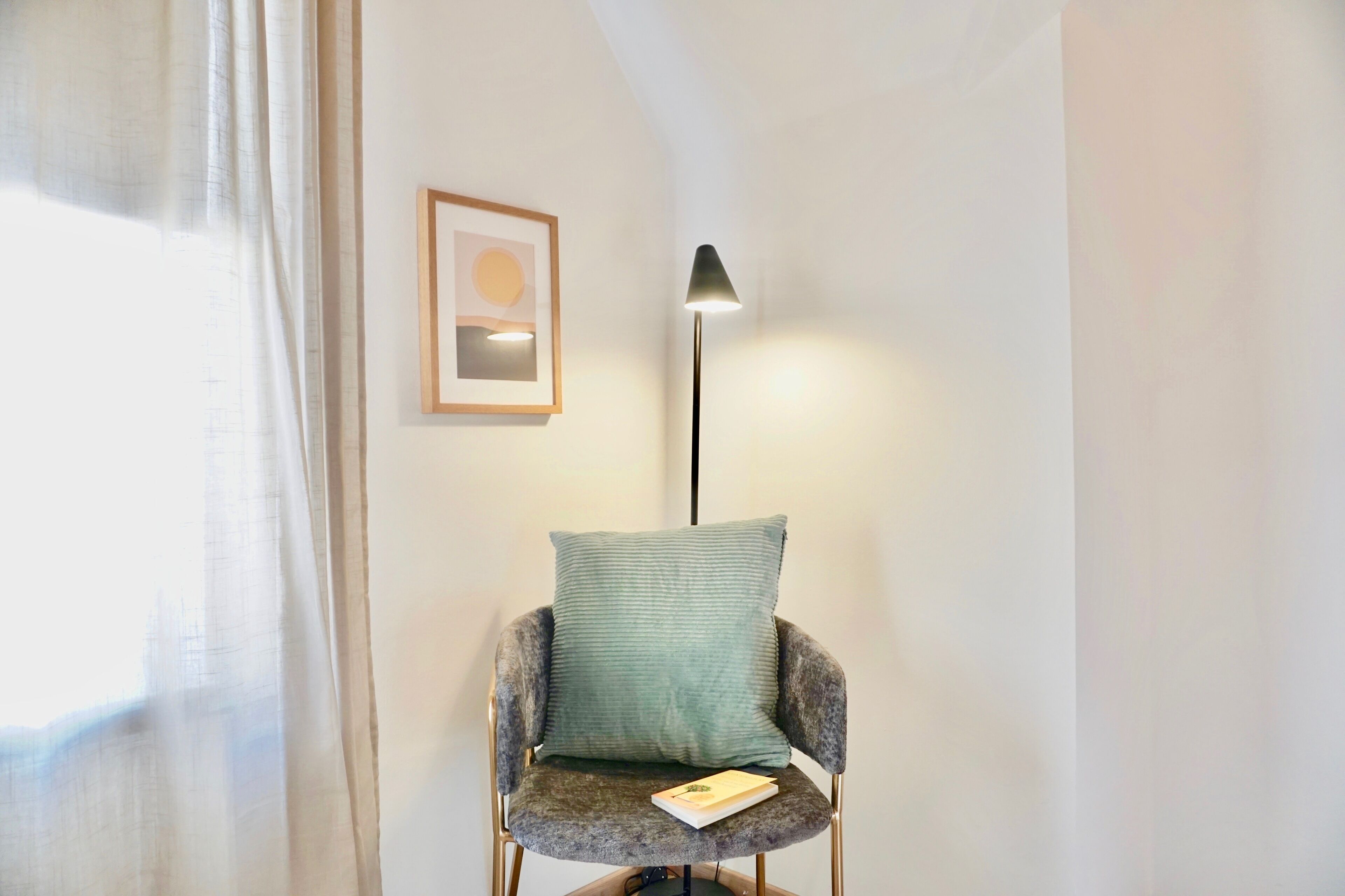 A chair with a cushion and a book, a floor lamp, and a framed picture on the wall.