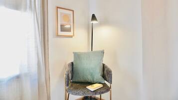 A chair with a cushion and a book, a floor lamp, and a framed picture on the wall.