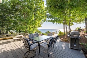 A deck with a glass-top table and chairs, overlooking a body of water.