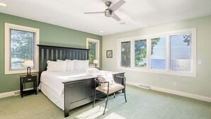 A bedroom with a bed, a chair, a nightstand, a ceiling fan, and large windows.