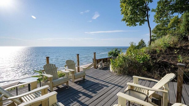 A wooden deck with Adirondack chairs overlooking a calm sea.