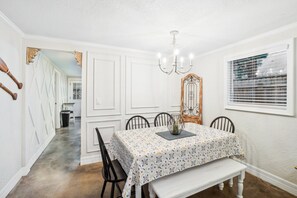 Comedor con una mesa preparada para cuatro, un candelabro y una ventana con persianas.