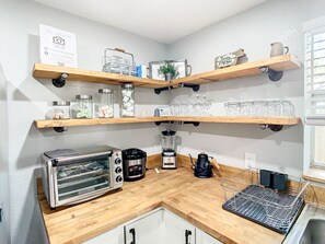 Una cuina amb prestatges de fusta que sostenen pots, una torradora, una cafetera i una batedora.