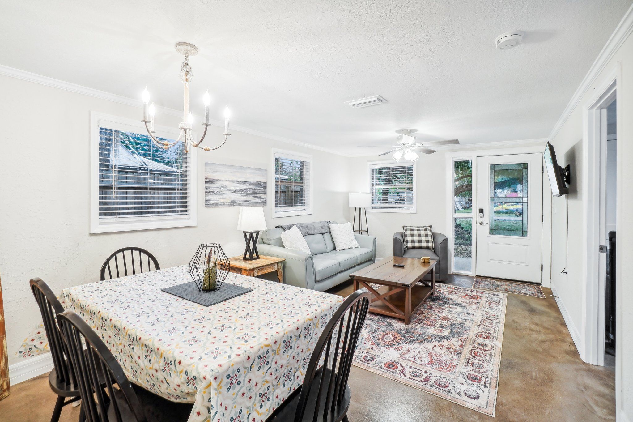 A spacious living room with a dining area, a grey sofa, a coffee table, and a chandelier.