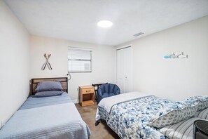 Een slaapkamer met twee eenpersoonsbedden, een nachtkastje, een stoel, een raam met zonwering en een deur.
