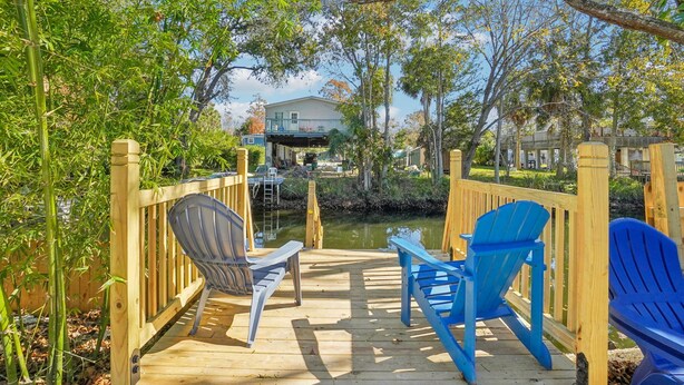 A wooden deck with chairs and a table, overlooking a body of water and a house. - Riverfront Retreat on deep canal with Hot Tub,  Clear Kayaks & Fire pit (Spring Hill)