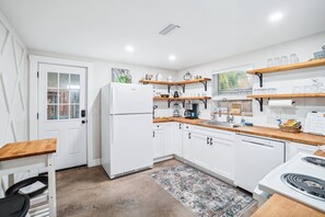 Una cocina moderna con armarios blancos, encimeras de madera y estufa integrada. Se puede ver un refrigerador, un lavamanos y varios electrodomésticos de cocina.
