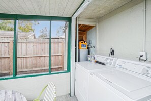 A laundry room with a large white washer and dryer, a wooden fence outside, and a green-framed window.