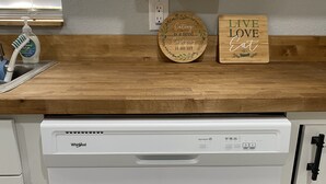 A kitchen with a white dishwasher, wooden countertops, a paper towel holder, a soap dispenser, and a wooden sign with the text "Live Love Eat". - Riverfront Retreat on deep canal with Hot Tub,  Clear Kayaks & Fire pit (Spring Hill)