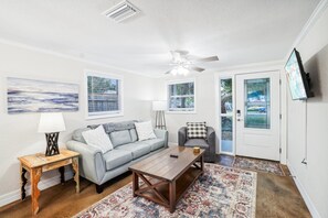Un salon comprenant un canapé, un fauteuil, une table basse et un téléviseur fixé au mur.