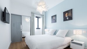 A modern bedroom with a bed, bedside tables, a TV, and a painting on the wall. - Florella Residences 2 pièces Antibes (Cannes)