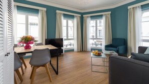 A modern living room with teal walls, a wooden floor, a dining table with chairs, a sofa, and a coffee table. - Florella Residences 2 pièces Antibes (Cannes)