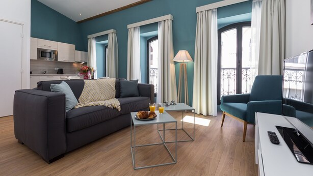 A modern living room with a sofa, a coffee table, and a TV. There is a kitchen in the background with a microwave and a kettle. - Florella Residences 2 pièces Antibes (Cannes)