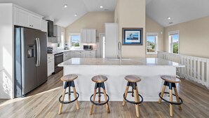 A spacious kitchen with a large island, stainless steel appliances, and wooden stools.