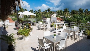 Une terrasse sur le toit, aménagée avec des espaces de détente en plein air, des plantes en pot et offrant une vue sur les palmiers et les bâtiments.