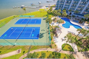 Luchtfoto van een hotel met een tennisbaan, zwembad en ligging aan het water.