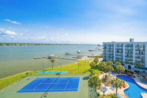 Een hotel met een tennisbaan, zwembad en uitzicht op het water.