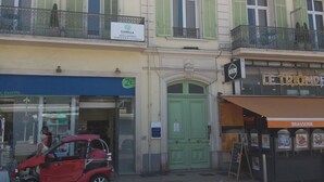 Een meerlaags gebouw met een bord voor appartementen 'Florella', een groene deur en een restaurant 'Le Triomphe' met terras.