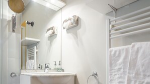 Een badkamer met een wastafel, spiegel, handdoekhouder en een prullenbak.