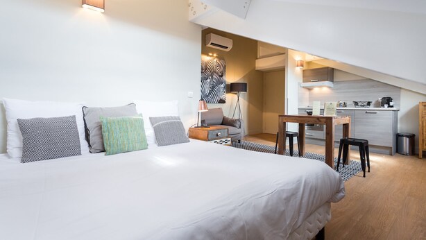 Een slaapkamer met een groot bed, een bureau en een kitchenette op de achtergrond.