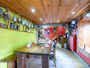 Un coin repas en bois avec une longue table dressée pour un repas, un escalier menant à un niveau supérieur et un mur rouge orné de divers objets.