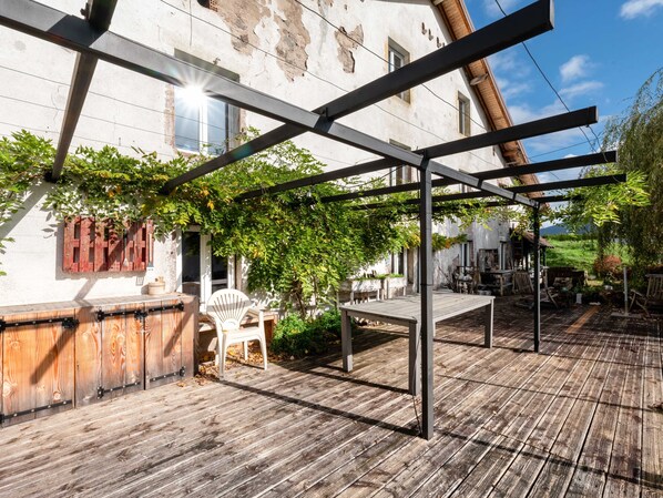 Une terrasse en bois agrémentée d’une pergola, entourée de verdure et de meubles rustiques.