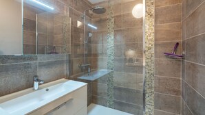 Une salle de bain moderne avec une douche à parois de verre, un lavabo blanc et un mur de douche recouvert de carreaux.