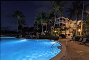 A swimming pool with lounge chairs and palm trees at night.