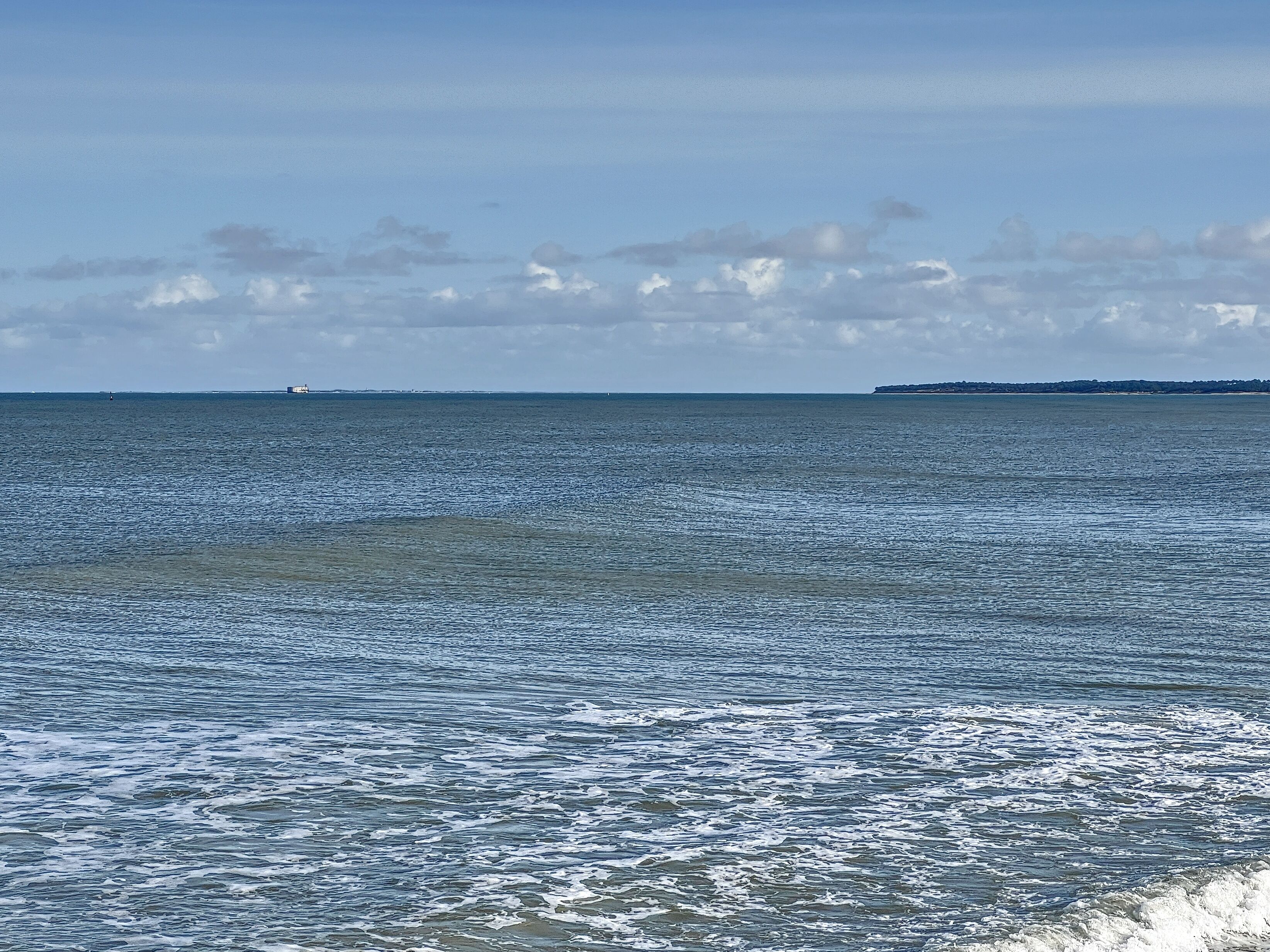 A coastal view with a calm sea, distant landmass, and overcast sky.