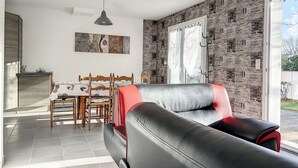 Una sala de estar moderna con un sofá de cuero negro, un comedor con mesa y sillas de madera, y un ventanal con papel tapiz estampado.