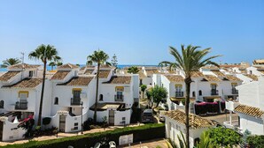 Una zona residencial costera con edificios blancos, palmeras y un cielo azul despejado.