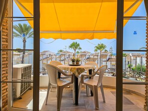 A balcony with a yellow awning, wicker chairs, and a table with a vase and wine glasses.